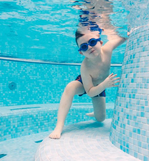 Young boy playing underwater in a swimming pool with goggles on. Recreation and leisure activities.