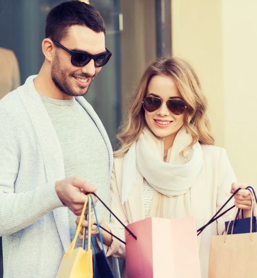 sale, consumerism and people concept - happy couple looking into shopping bag at shop window on city street