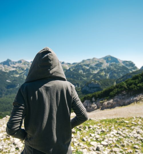 Mountain hiker at high viewpoint looking at the valley. Female tourist person in hooded jacket at mountain top enjoying the view.
