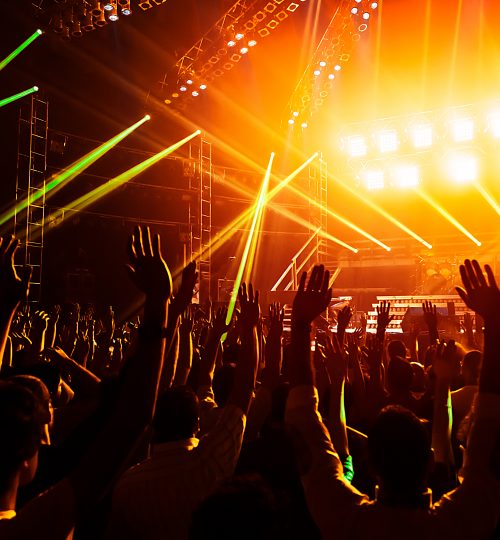 Photo of young people having fun at rock concert, active lifestyle, fans applauding to famous music band, nightlife, dj on the stage in the club, crowd dancing on dancefloor, night perfomance