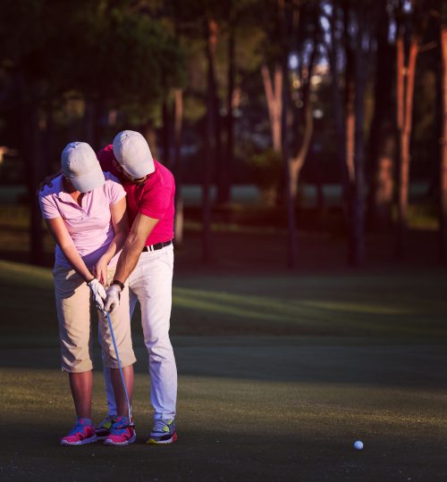 male golf instructor teaching female golf player, personal trainer giving lesson on golf course