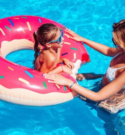Little girl with her mom having fun in swimming pool.