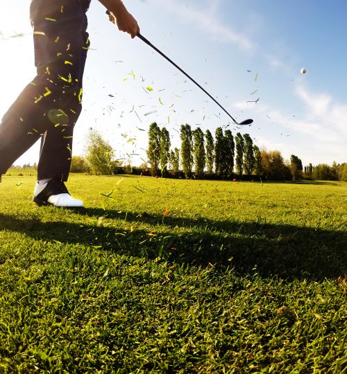 Golfer performs a golf shot from the fairway. Sunny summer day.