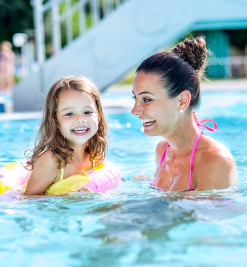 Young beautiful mother in bikini playing with her daughter in inflatable ring in swimming pool in aqua park. Summer heat and water.